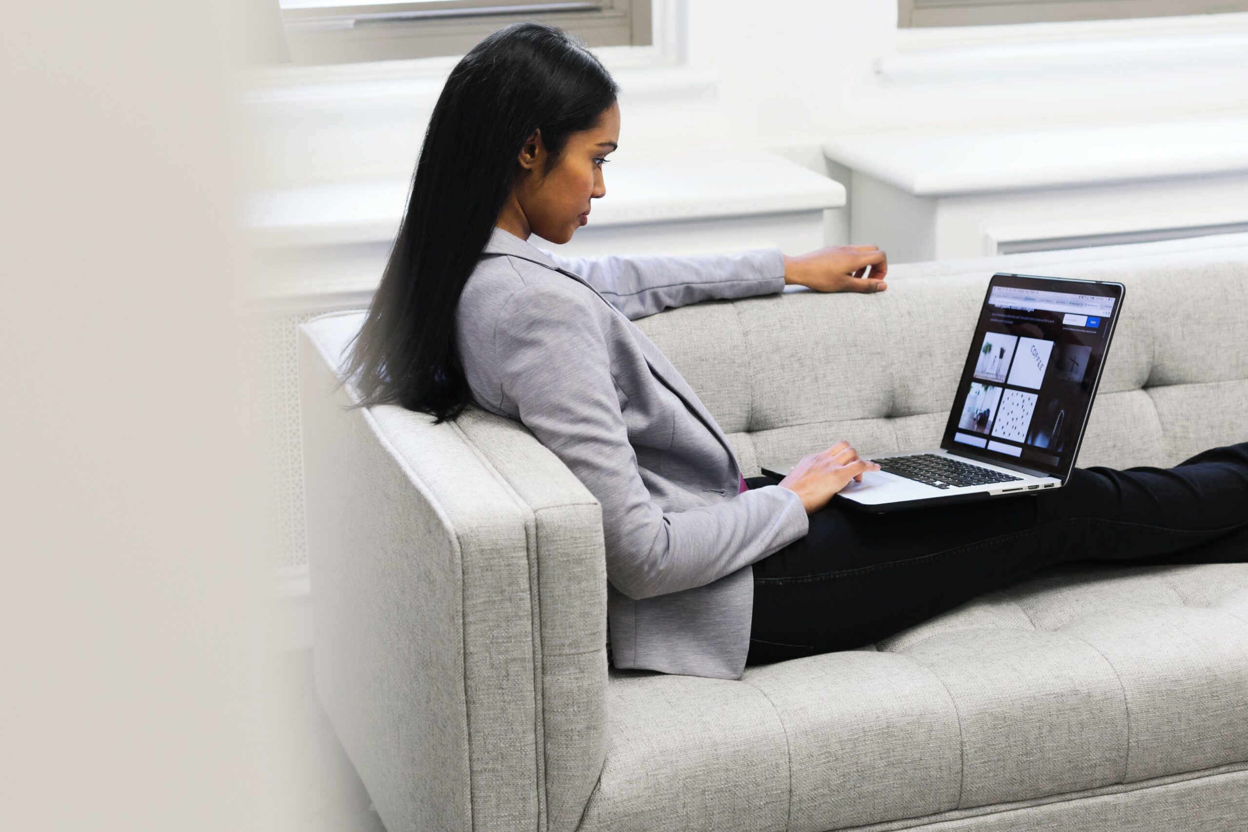 Casually sitting on a couch, a woman checks out how to export as an entrepreneur on her laptop