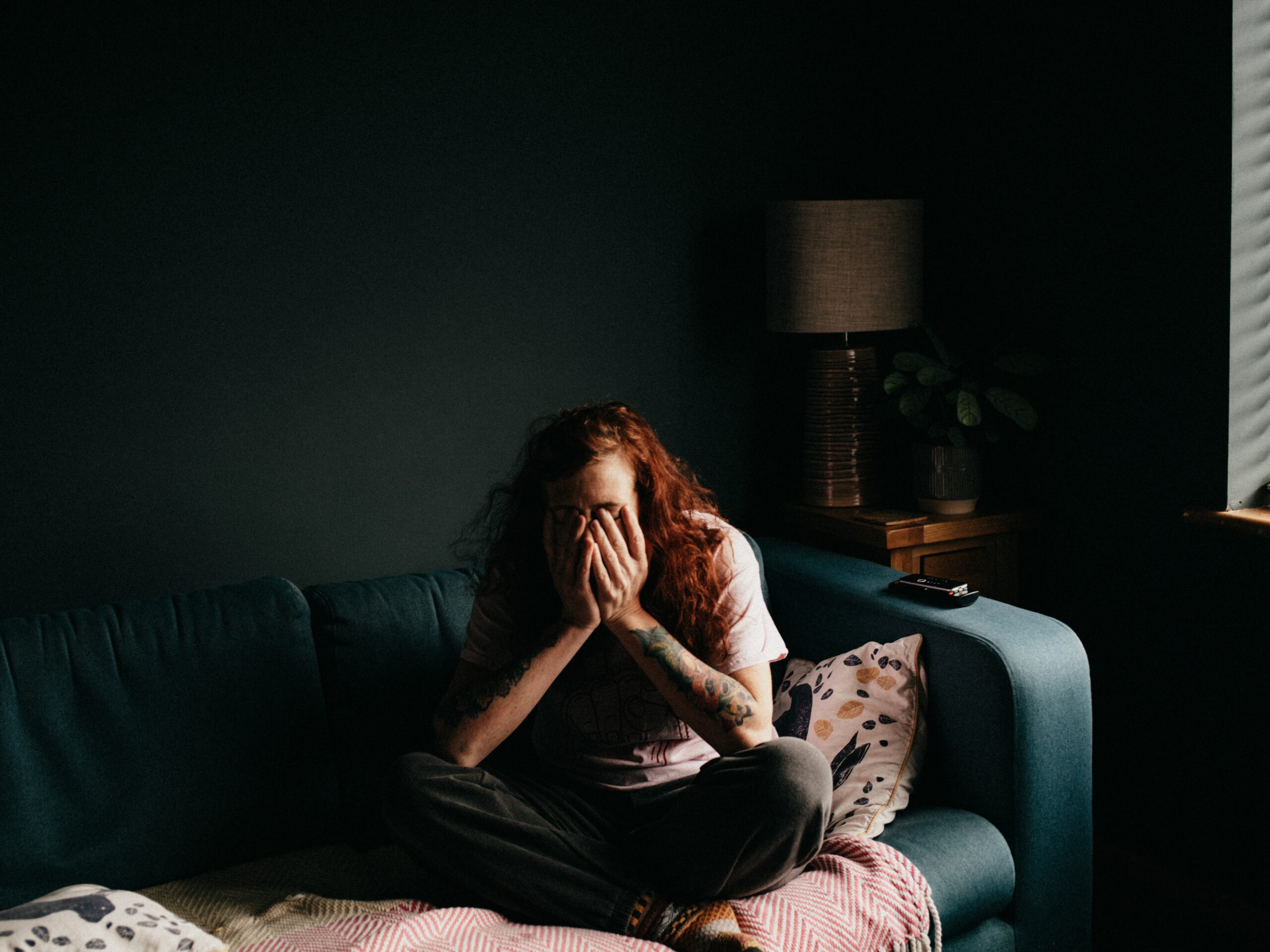 A person sitting on the couch in the dark with hands on their face