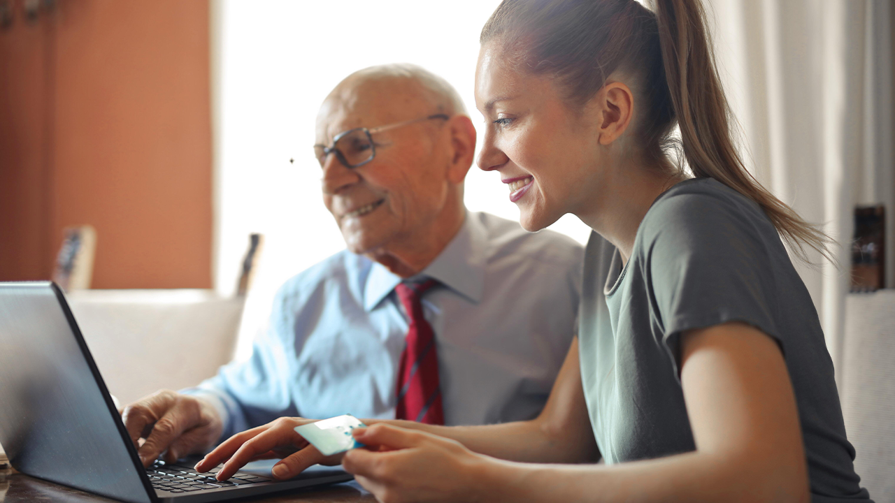 Business man sitting next to woman colleague who is helping him with his laptop