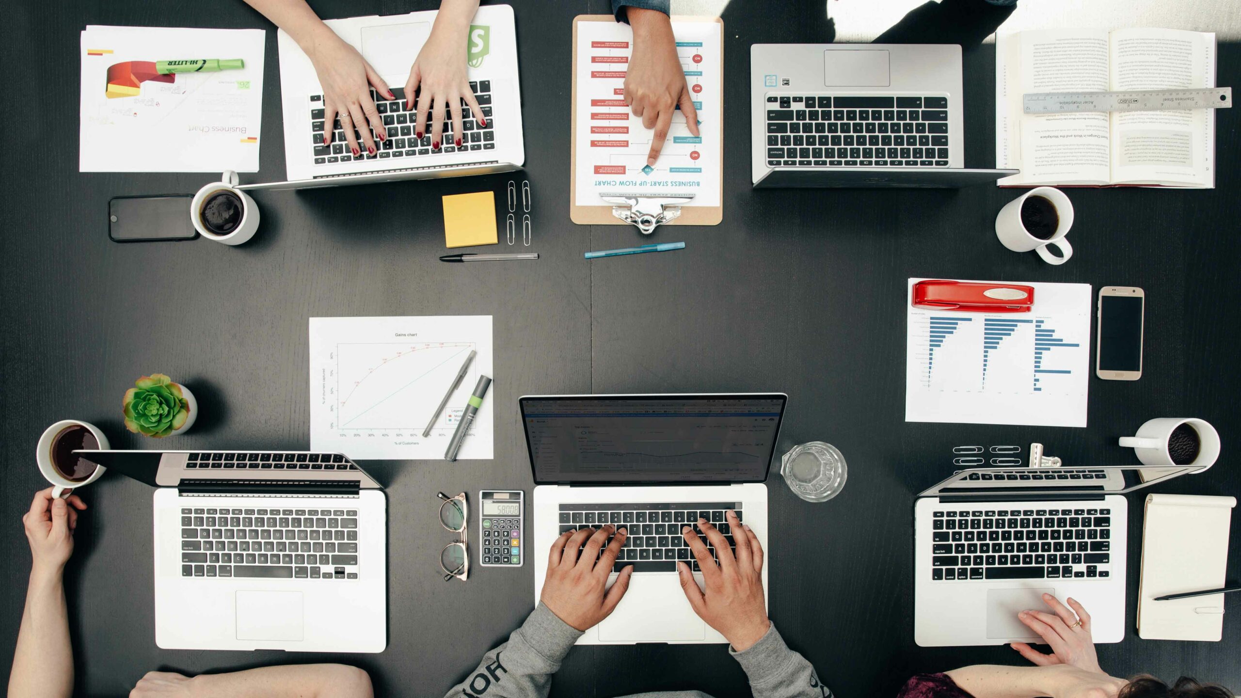 Overhead shot of five people working at a table on laptops